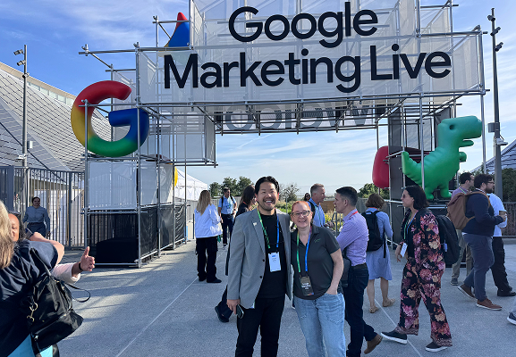 People stand and pose for photos outside the entrance to Google Marketing Live, with a large event sign and Google-themed decorations visible.